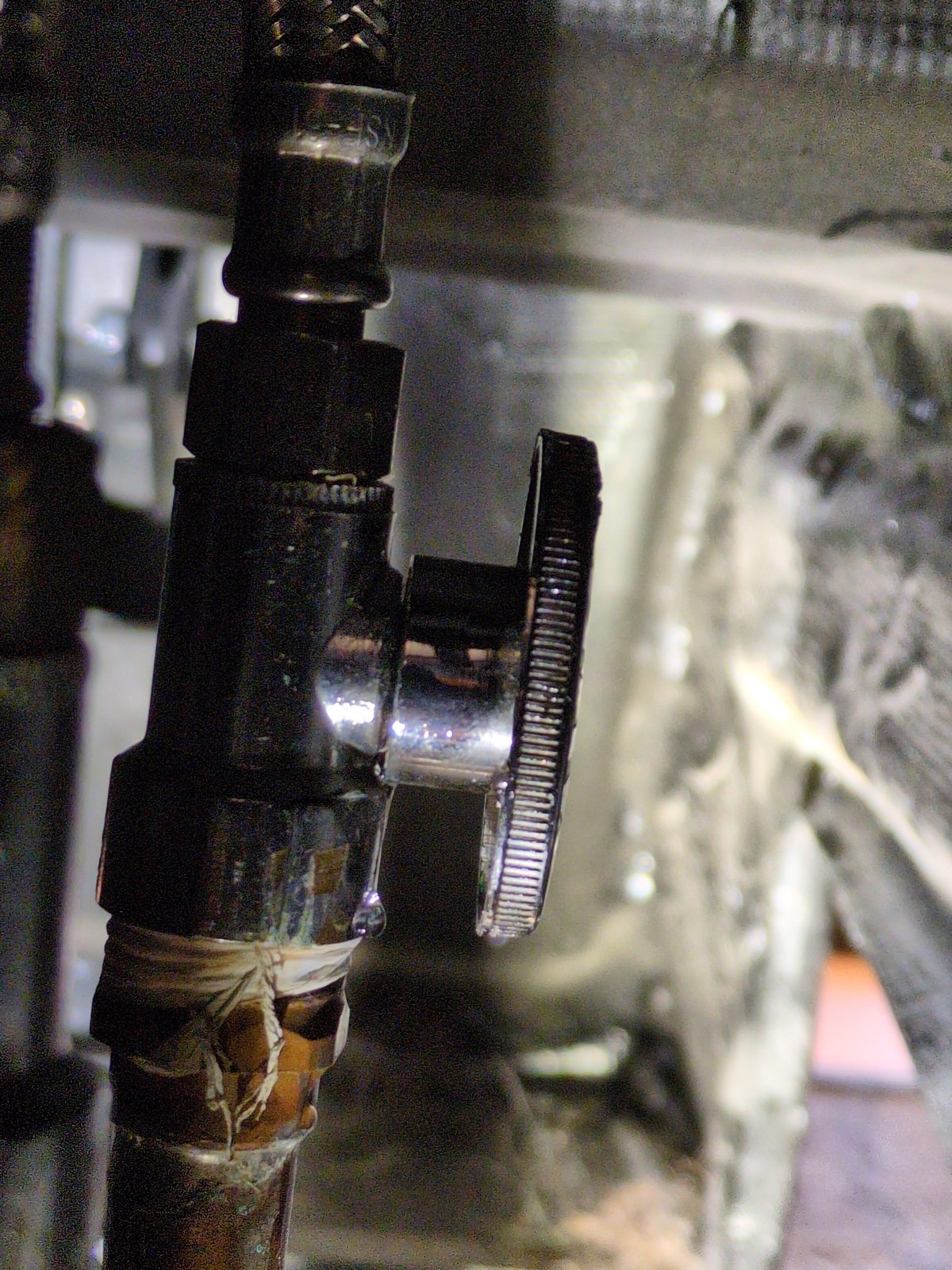 Close-up of an aging chrome angle stop valve with corrosion and a water droplet forming beneath the connection