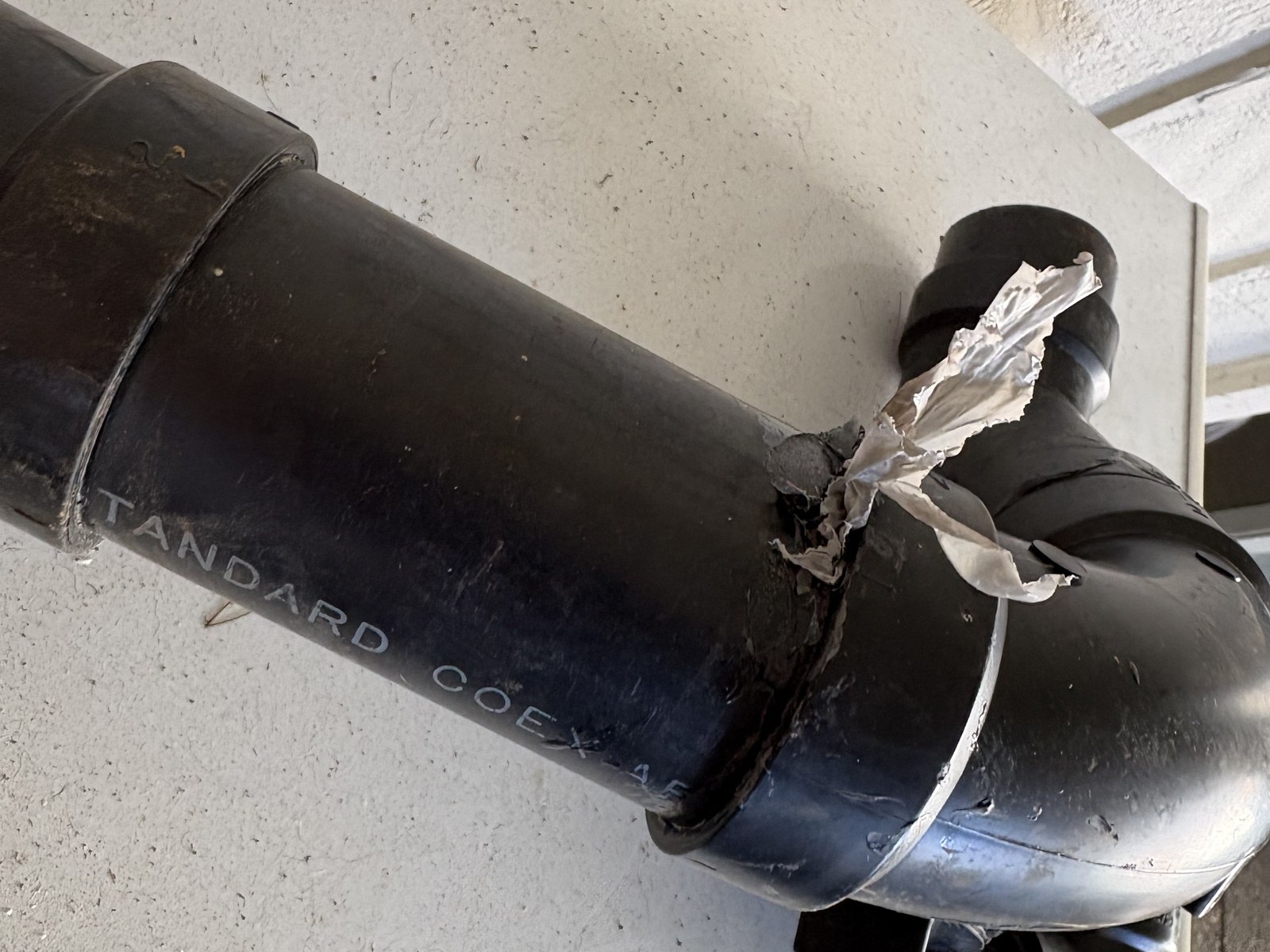 Black ABS drain pipe and elbow on a white surface, with a torn strip of clear plastic sticking out of one joint