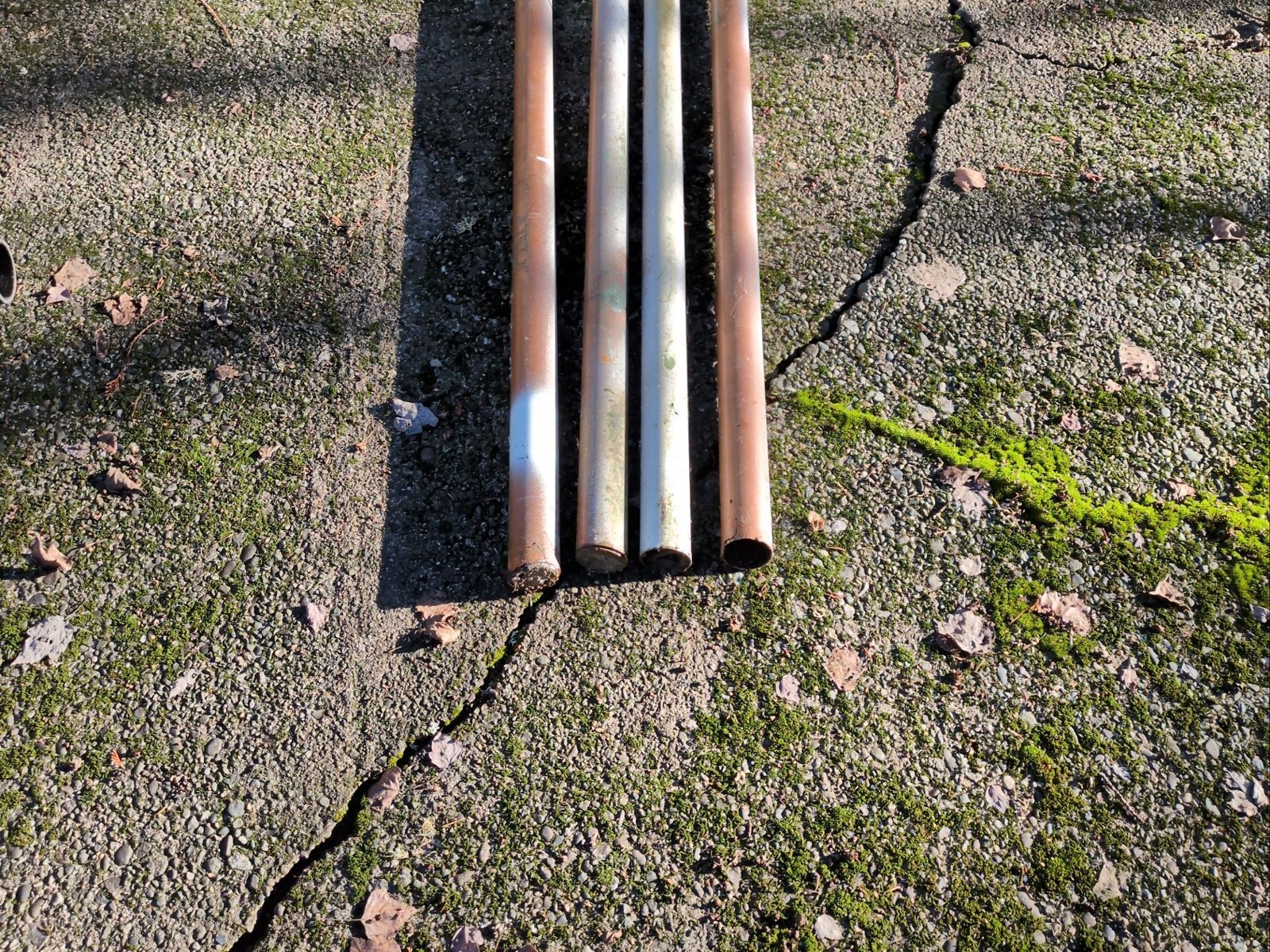 Four lengths of old rusted and gray metal pipe laid side by side on a mossy concrete patio