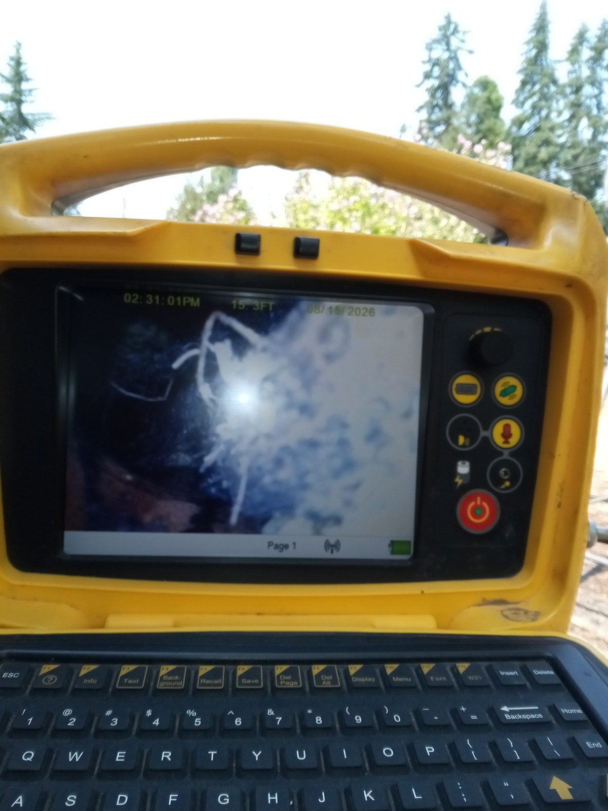 Sewer camera monitor on site showing the inside of the pipe with fine roots visible and a distance counter reading just over fifteen feet