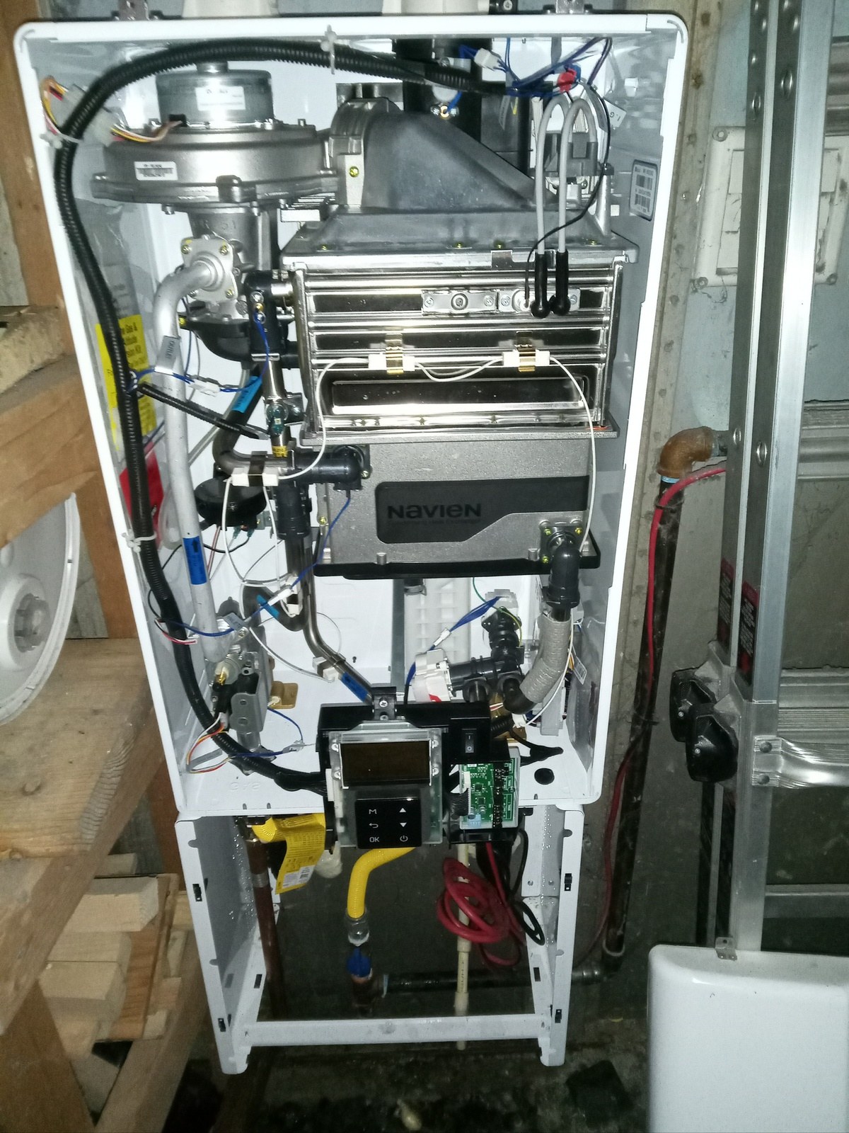 Navien tankless water heater with the front cover removed showing the fan, burner assembly and heat exchanger during service