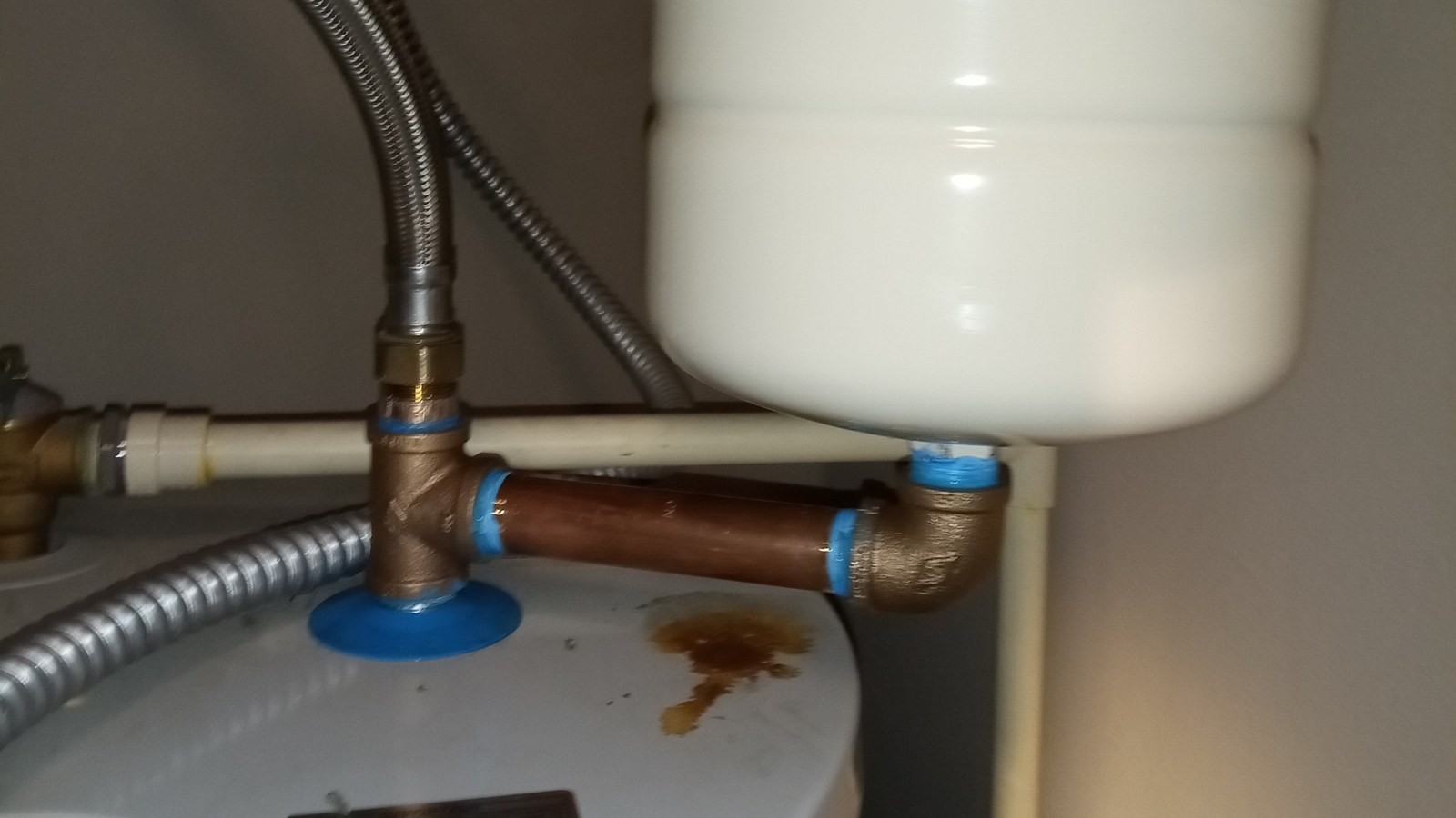 New brass fittings and a copper nipple on top of a water heater, connected to a white expansion tank on a short pipe, with braided flexible lines above