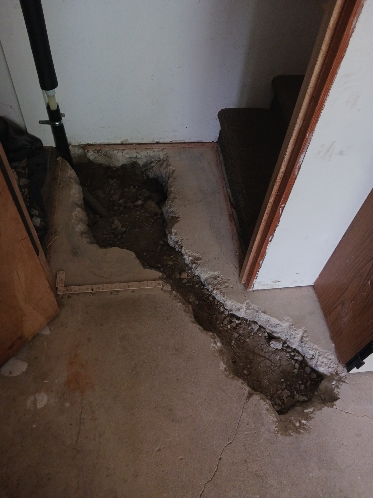 Concrete slab floor cut open in a trench through a hallway, exposing soil and the old water line beneath a Bellevue home