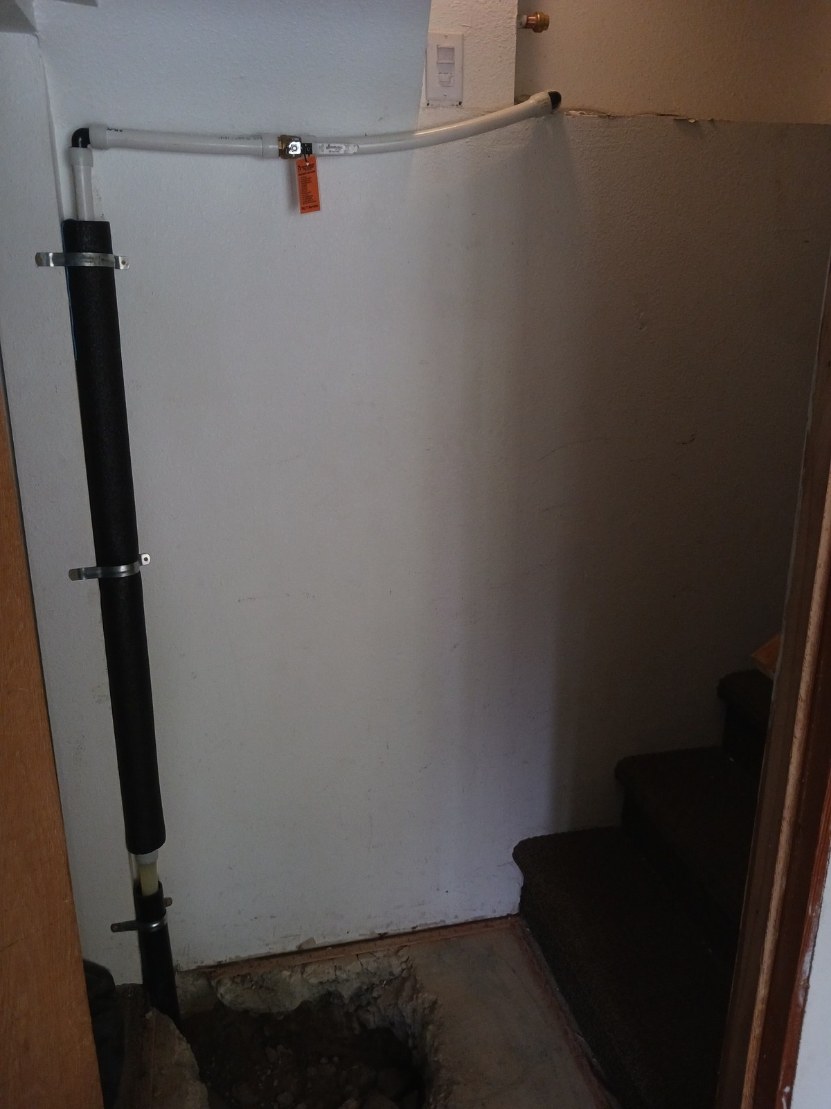 New insulated water line rising through the slab in a stairwell corner, strapped to the wall with a new shutoff valve and service tag