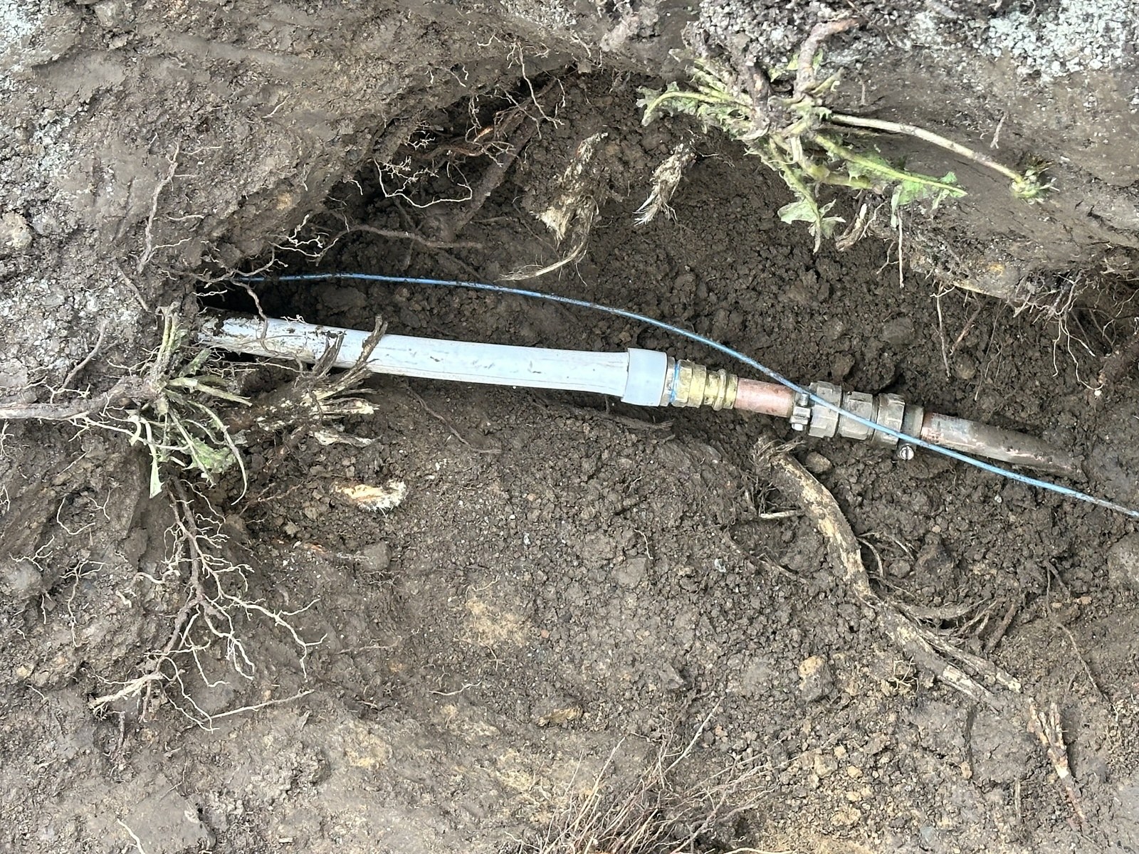 Close view of a new water service spliced to existing copper with brass fittings in an open excavation with roots in the soil wall