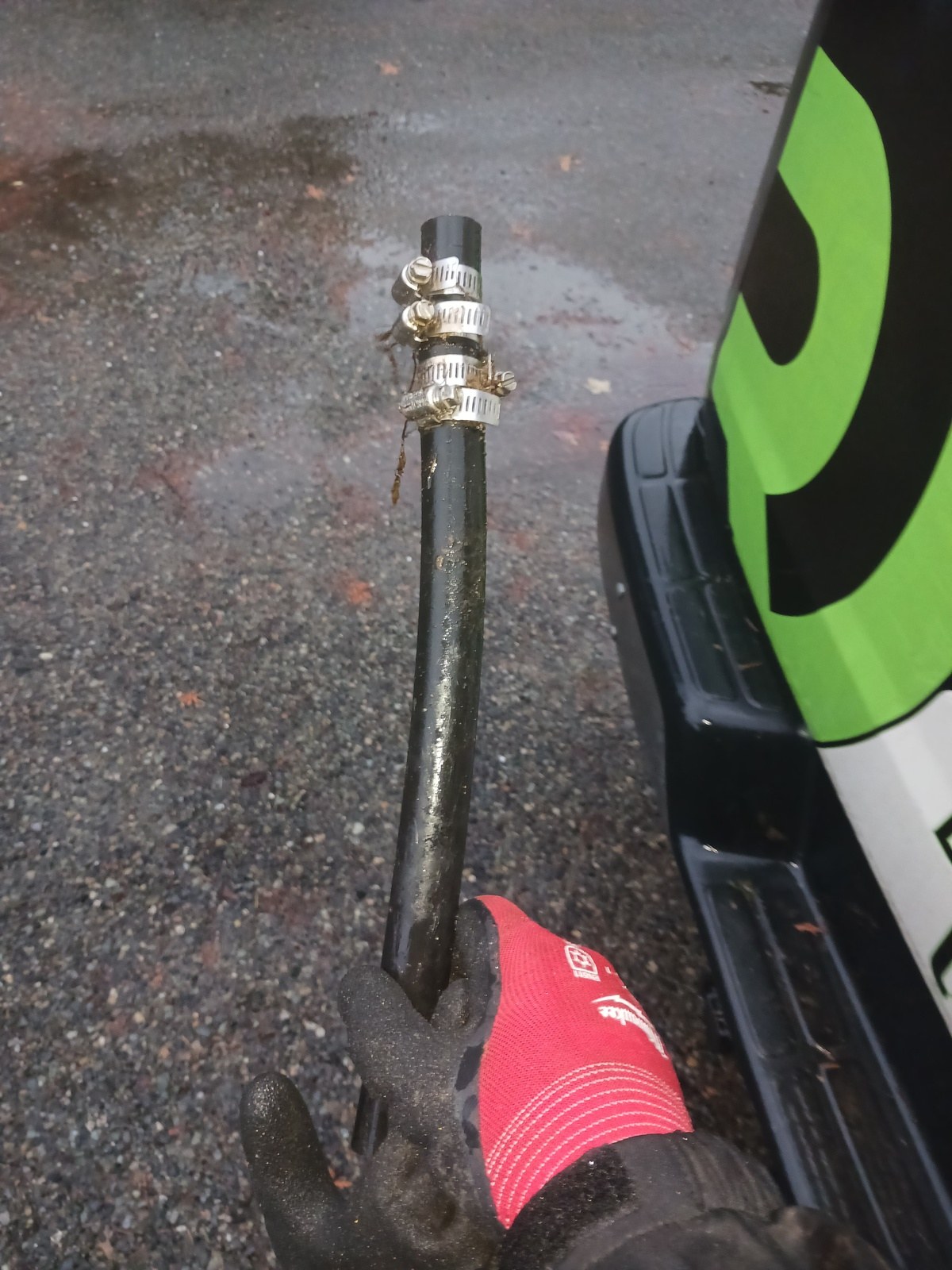 Gloved technician holding a removed section of black poly water line with two pairs of stacked hose clamps beside a service van